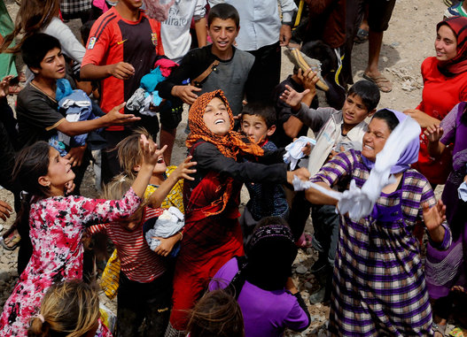 Displaced Iraqis catch clothes provided by a charity outside the Bajid Kandala camp in Feeshkhabour, Iraq on Aug. 19, 2014. (AP Photo/Khalid Mohammed)